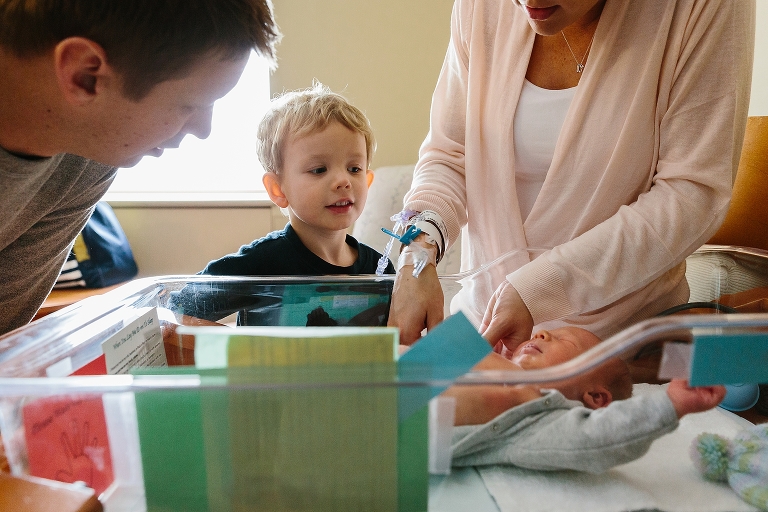 Young boy watches newborn baby brother in the hospital with parents