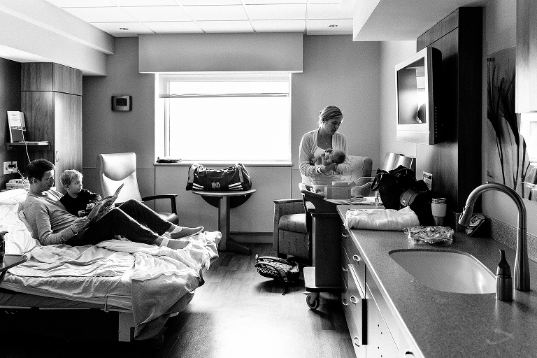 Black and white, Father reads book to son while mom puts baby to bed in hospital