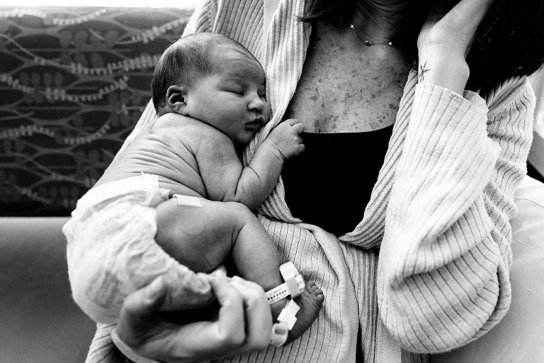 Black and white. Sleeping newborn baby holds mothers chest in hospital.