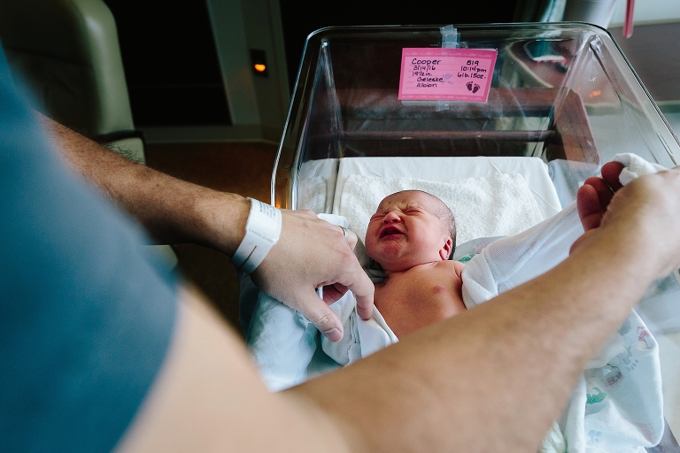 Father dresses newborn baby in hospital bed. 