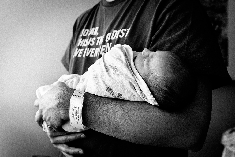 Father holds swaddled newborn baby in hospital.
