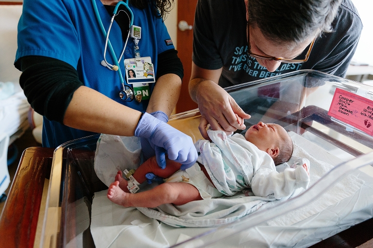 Nurse gives newborn baby a shot while father holds baby's hand