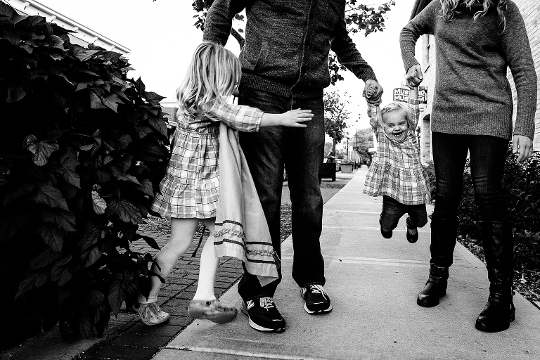 Black and white. Family of four walks down the sidewalk together.