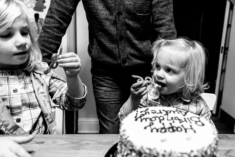 Black and white. Two little girls lick the candles from a birthday cake.