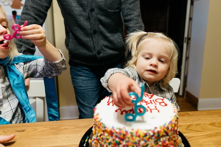 Two little girls lick the candles from a birthday cake.