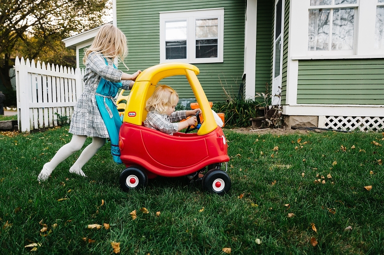 Little girl pushed her younger sister through the grass in a toy car in their yard