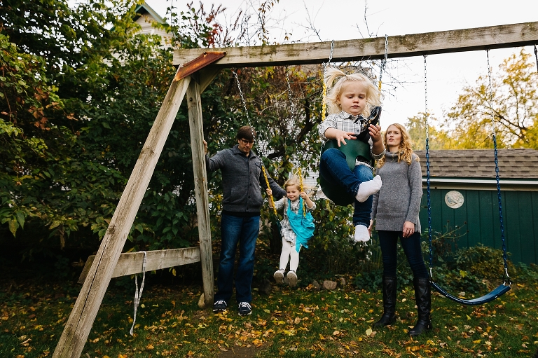 Father and Mother push their daughters on the swing set
