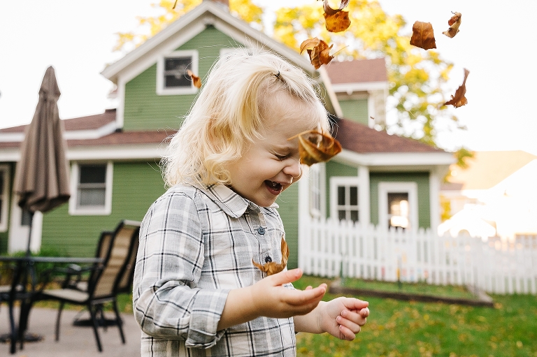 Little girl laughs playing outside throwing leaves in the air.