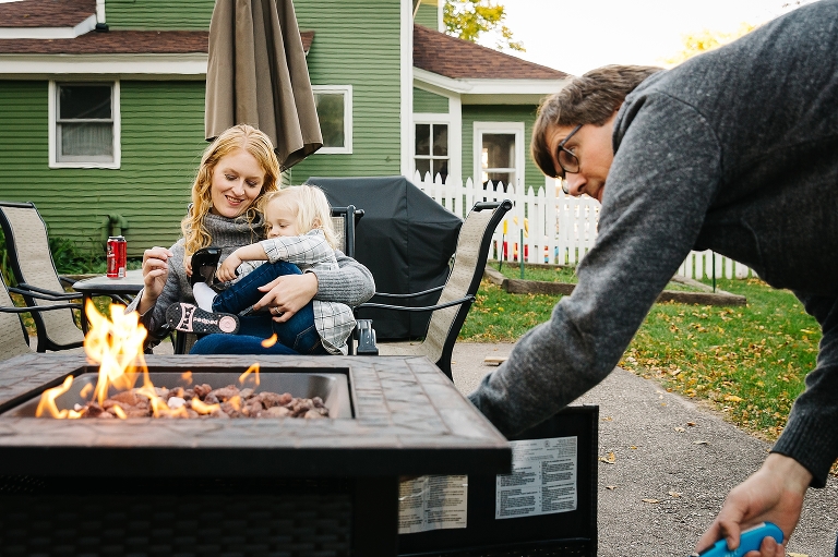 Mother sitting outside in hair with daughter while father lights the firepit