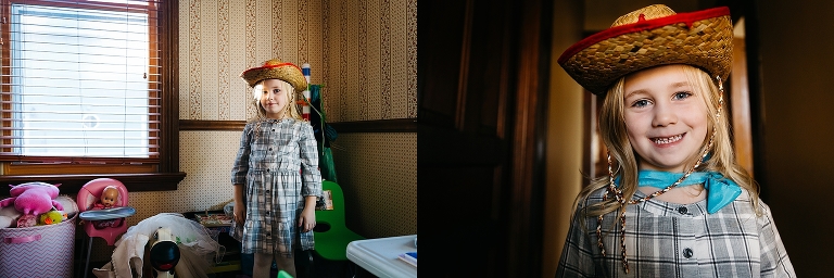 Young girl wearing plaid dress and cowgirl hat stands in her playroom.