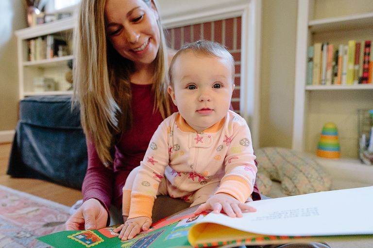 Baby girl looks at a book on her mother's lap