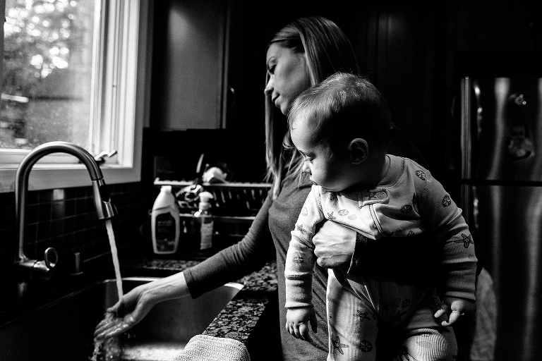 mother tests water temperature in sink while holding baby daughter 
