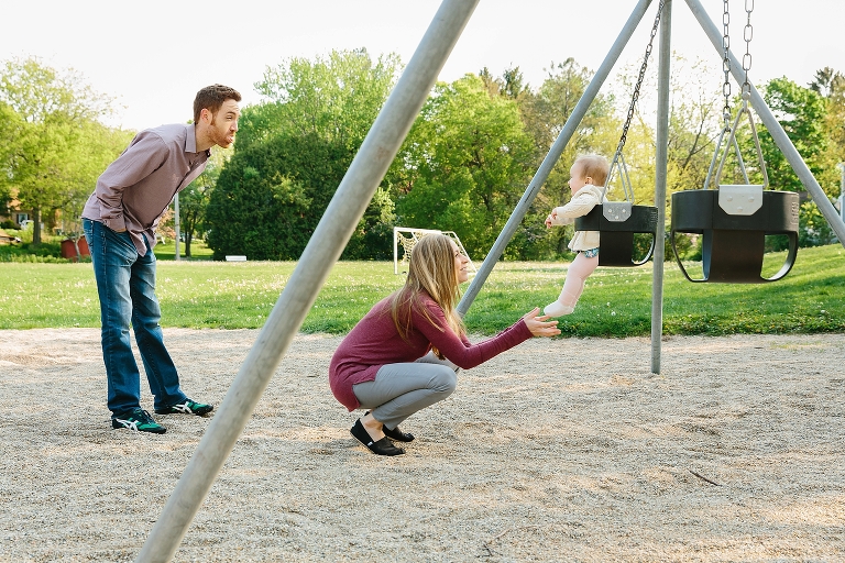 Baby 7 month old girl plays on a swing as parents engage with her