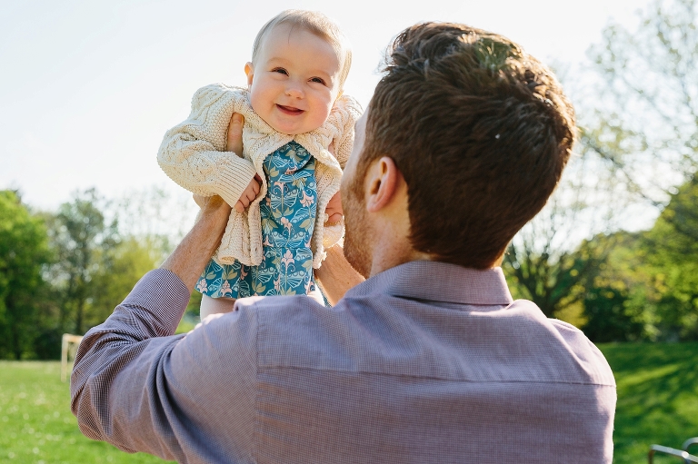 Dad lifts up 7 month old girl on a sunny day at the park 