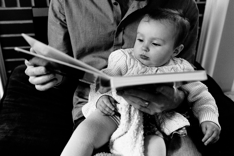 Portrait of 7 month old sitting on dad's lap, listening to a story during a Sunday morning pancakes photo session