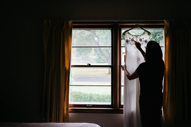 Wedding dress hanging on window with woman standing looking at it