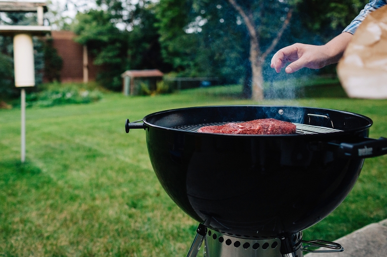 Man seasoning piece of red meat cooking outside on grill