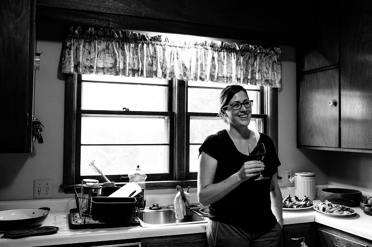 Black and white. Woman standing in kitchen next to sink laughing holding glass of wine