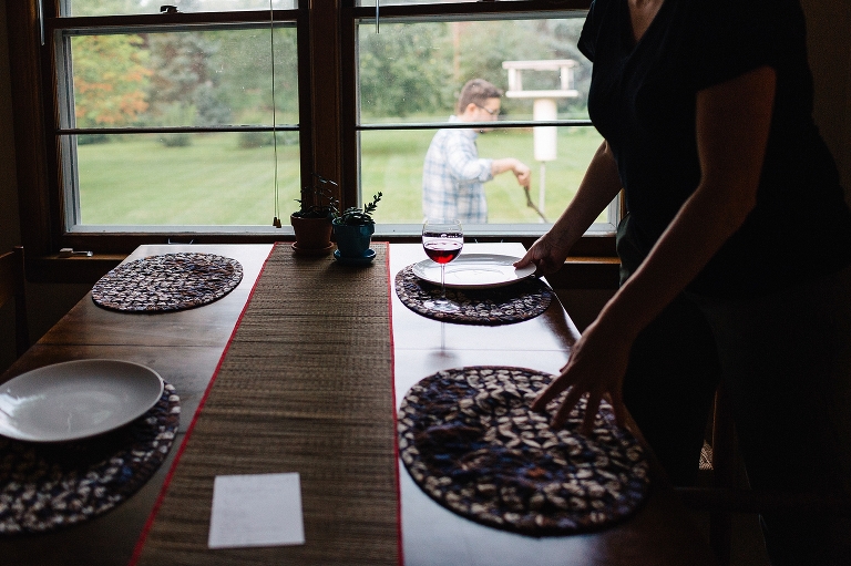 Dinner table set with placemats and plates outside window see man grilling dinner