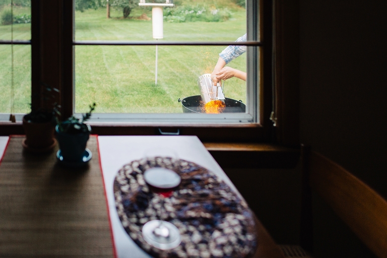 table setting next to window with man grilling outside pouring glowing hot embers into grill