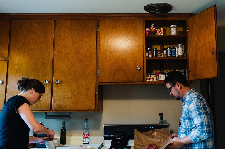 Man and woman cooking in kitchen together. wood cabinet door open full of spices.