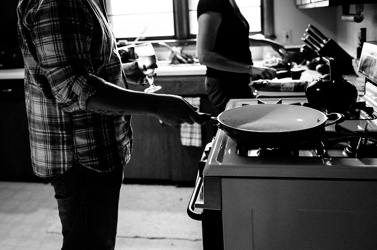 Black and white. Two people cooking dinner in kitchen Man cooking rice on stove with beer in hand and woman prepping veggies.