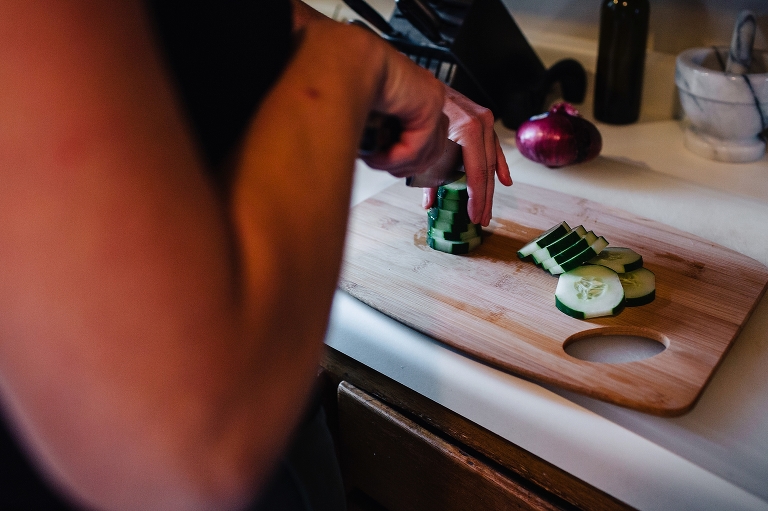Woman cooking in kitchen slices pieces of cucumber on cutting board.