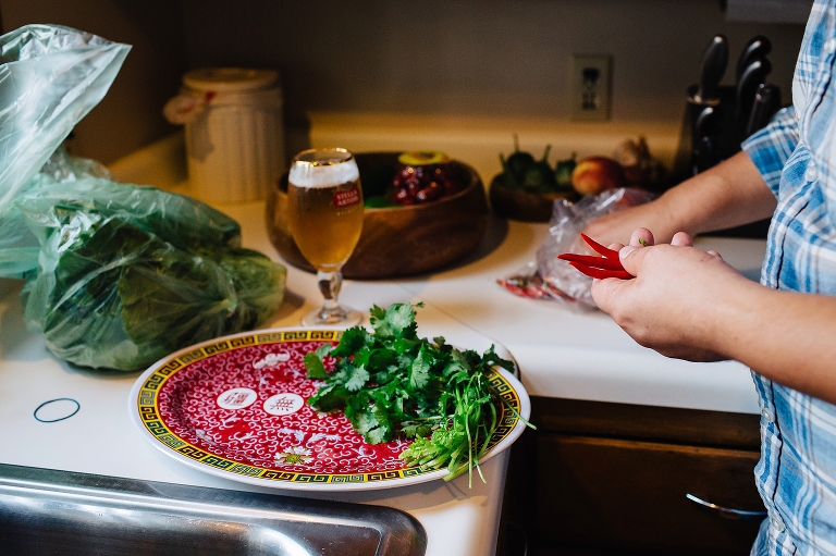 Man cooking in kitchen picks up peppers with cilantro on a plate and glass full of beer