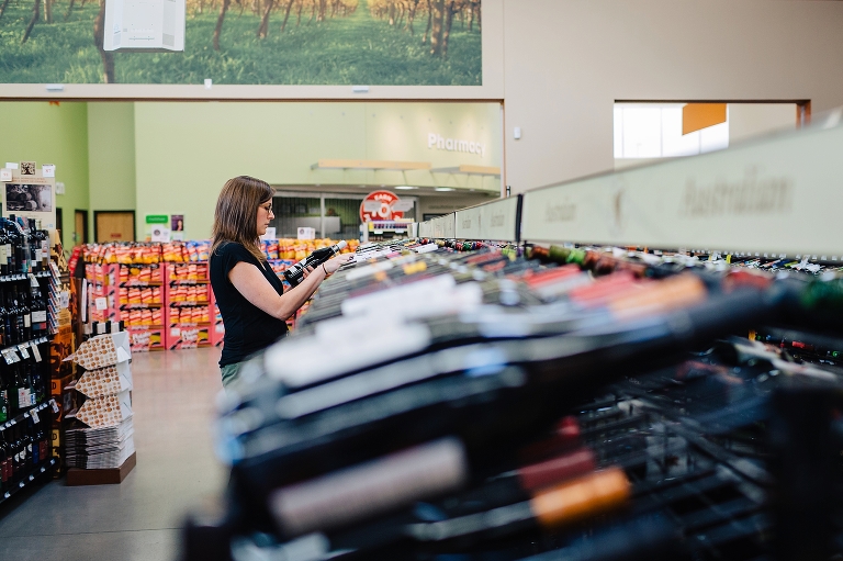 Woman in grocery store looks at bottle of wine