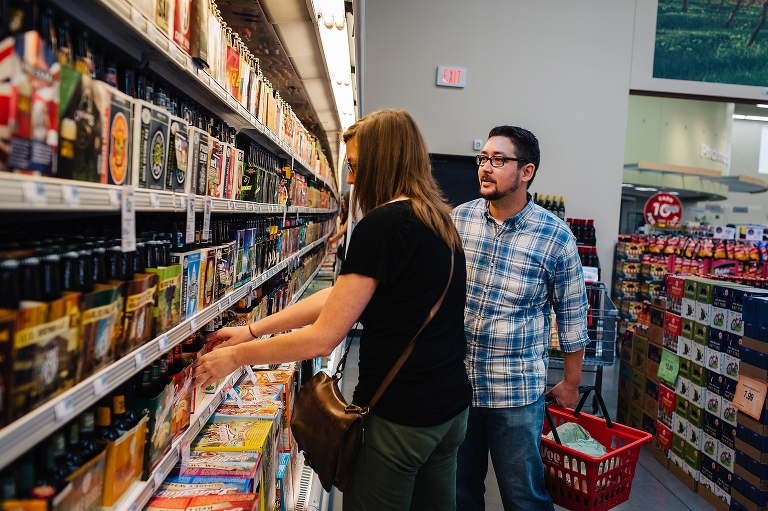 A couple grocery shopping picks out a package of beer