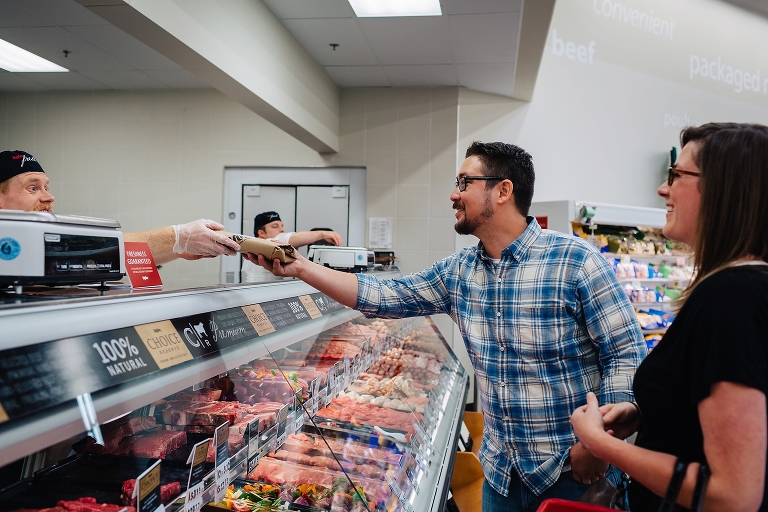 Butcher hands a package of meat to a couple grocery shopping.