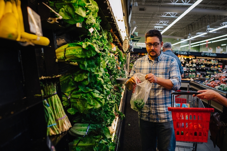 Man in grocery store puts bag of produce into shopping basket.