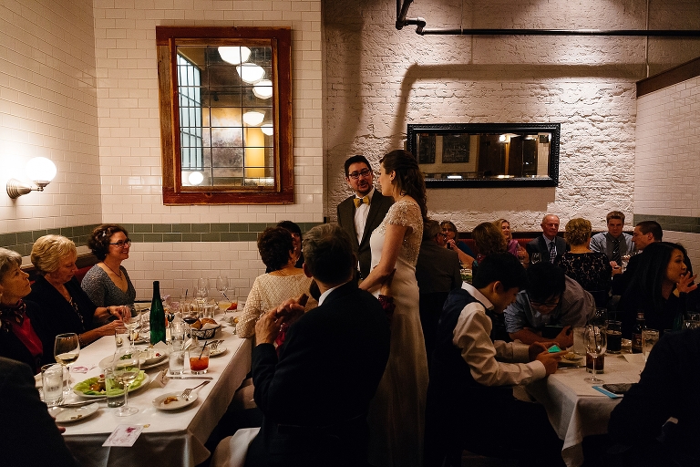 Bride and groom stand with family at wedding dinner