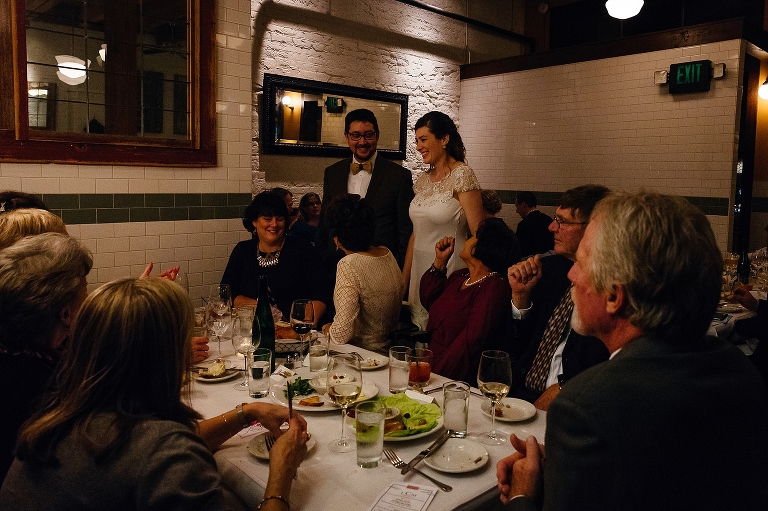 Bride and groom stand with family at wedding dinner