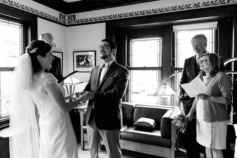 Black and white. Bride and groom laugh at their wedding ceremony, parents watch.