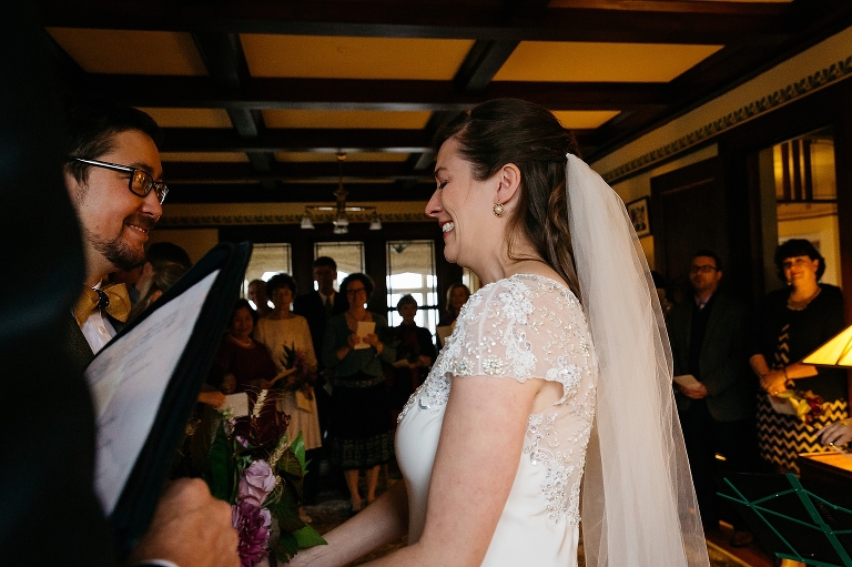 Bride holds grooms hand at the alter of their wedding. family smiling in the background