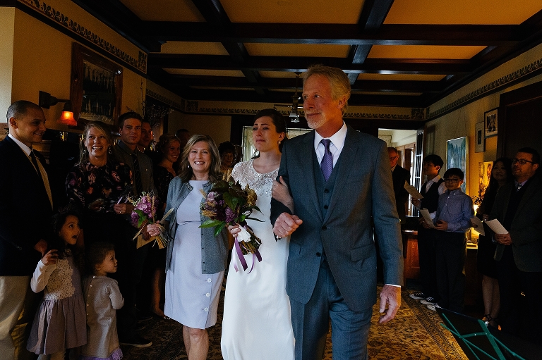 Father and mother walk the bride down the aisle, family smiling and watching