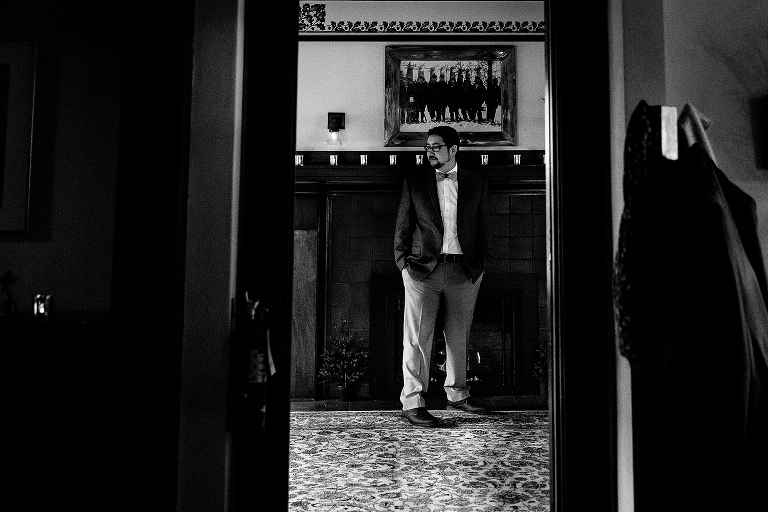 Black and white. Groom stands dressed and ready for his wedding