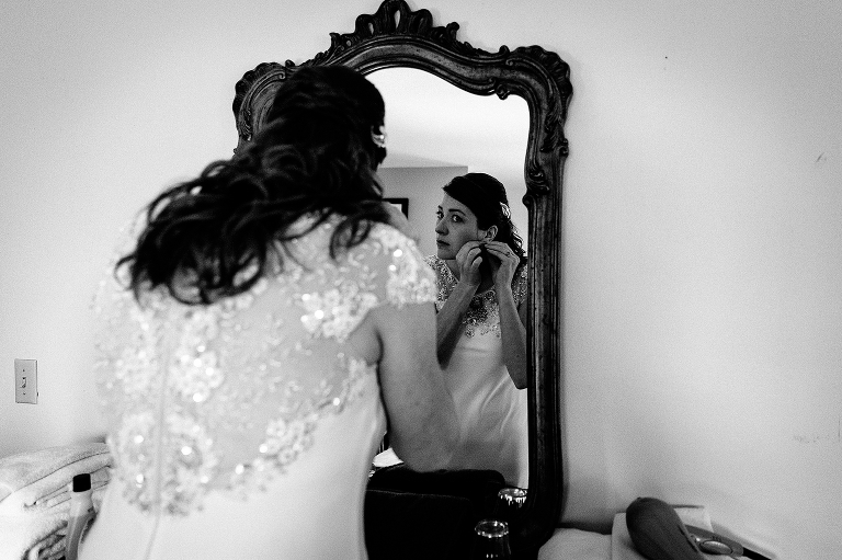 Black and white. Bride wearing wedding dress puts on earrings