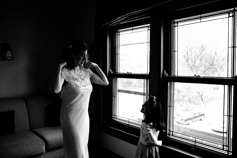 Black and white. Bride puts on wedding dress while talking to little girl