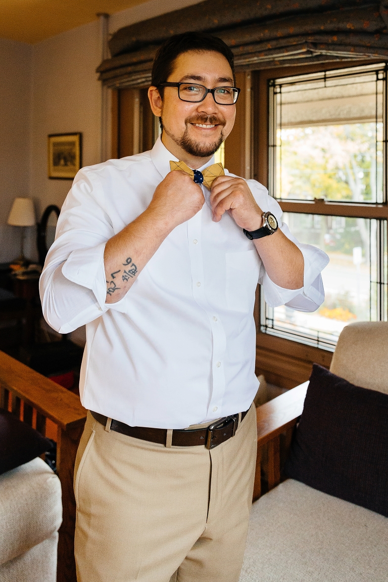 Groom puts on bow tie getting ready for his wedding