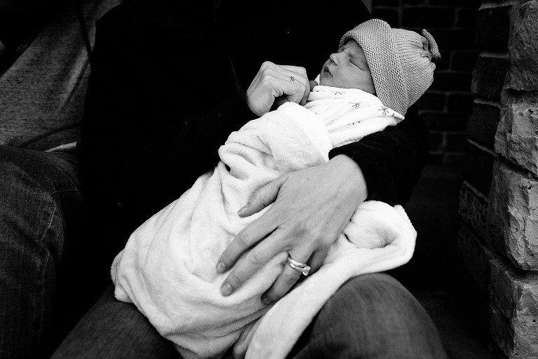 Mother holds sleeping newborn front steps 
