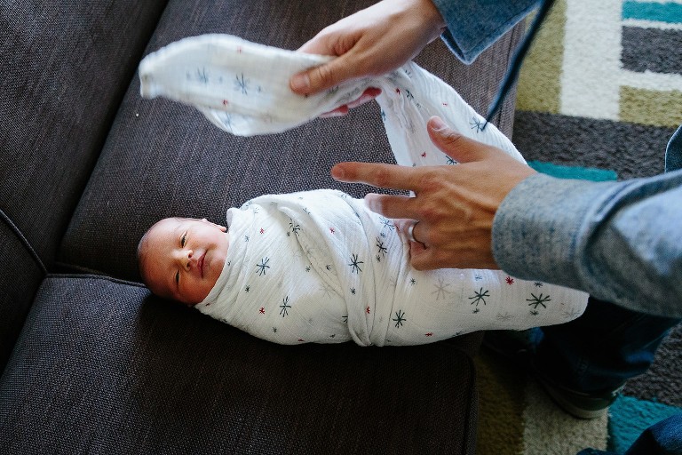 Dad swaddles newborn girl on couch 