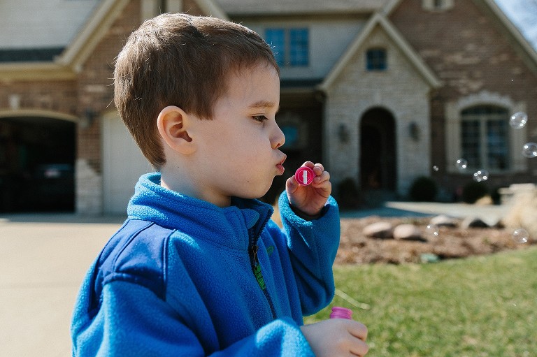 Boy blows bubbles in front house on cool early, spring day