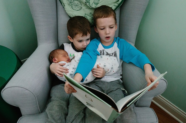 Two brothers hold newborn sister and read a story 
