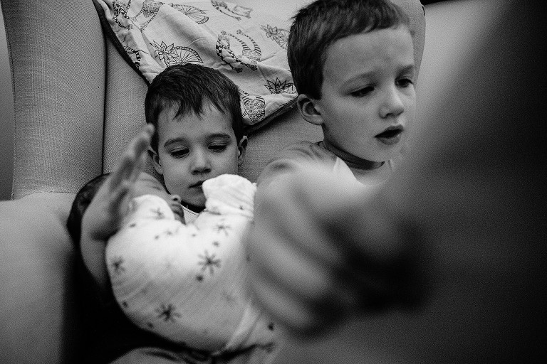 Black and white. Two brothers hold newborn sister and read a story 