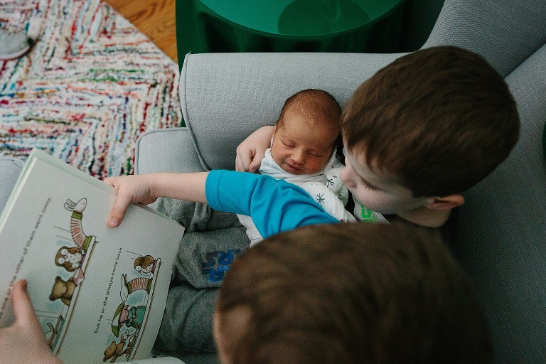 Two brothers hold newborn sister and read a story 