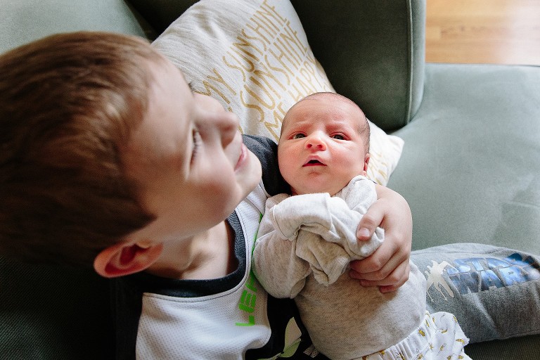 Big brother holds baby newborn sister on the couch 