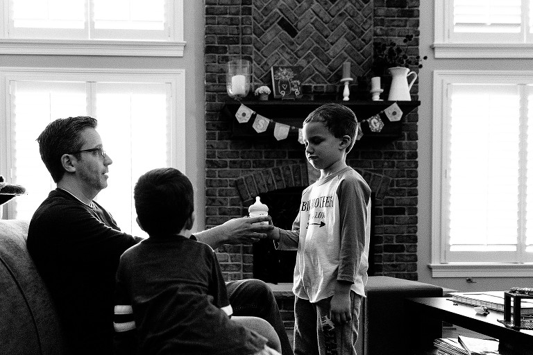Dad hands bottle to older brother, who isn't thrilled about the task 
