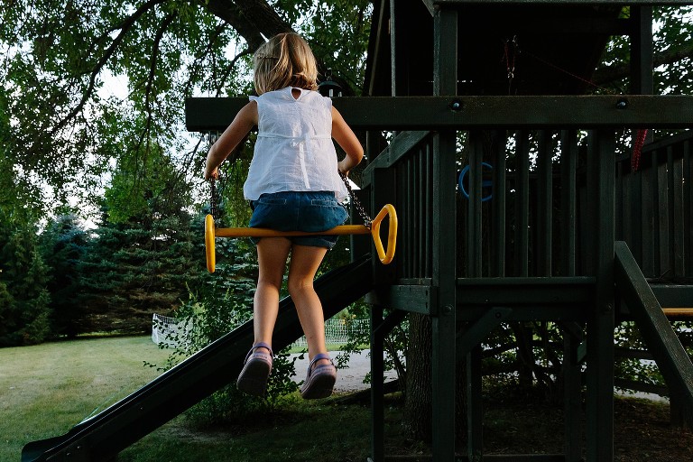 Girl sits on swing on a play structure at the end of the day.